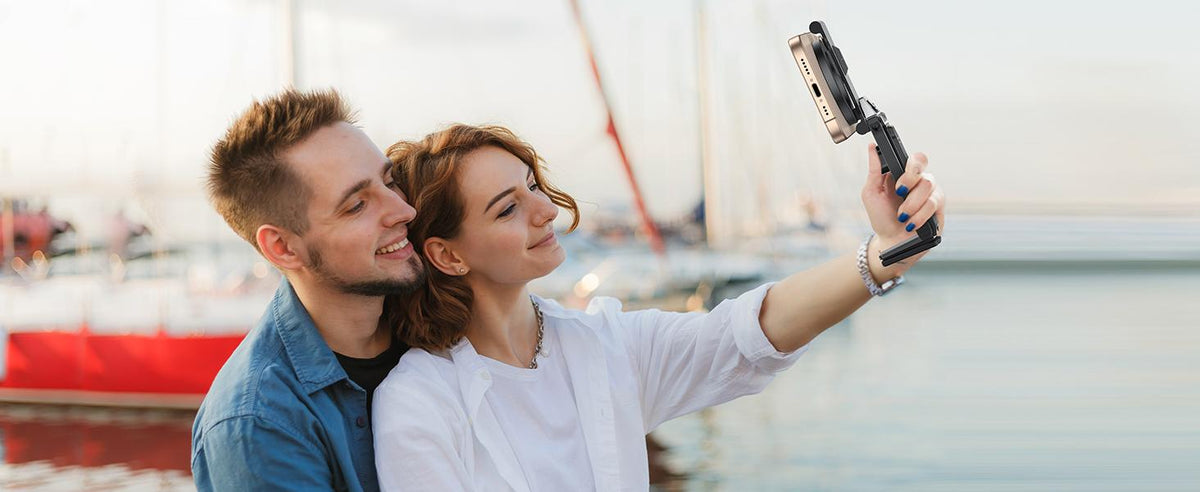 Couple taking a selfie outdoors near the water using a handheld magnetic phone tripod stick.